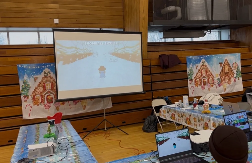 Penguin Game running on a projector at a holiday showcase, beside gingerbread-house posters